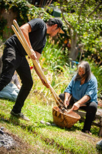 Mother and son team Jennifer and Carson Bates (Northern Sierra Mewuk) cooking Nupa (Acorn soup) by placing hot rocks in the porridge in a traditional handwoven basket at the 2nd Annual California Native Ways Festival. 21 June 2021, Berkeley, California. Photo by Austin Stevenot, (Northern Sierra Mewuk)